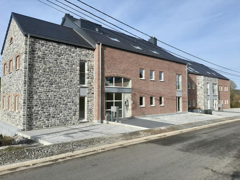 Dieses Projekt entsteht an der Stelle eines traditionsreichen Bauernhofes und umfasst 2 Residenzen mit insgesamt 12 Appartements und 5 Reihenhäusern (Doppel- und Dreierblock).
Die Appartements in den Residenzen erstrecken sich auf 3 Ebenen und verfügen über u.a. Aufzüge, unterirdische Parkplätze, einen Balkon und eine unschlagbare Weitsicht.
Bei dieser Wohnung handelt es sich um ein Appartement auf der ersten Etage mit Eingangsbereich, 2 Schlafzimmern, Living, Küche, Abstellraum, Bad, separates WC und einer Terrasse.
Gasheizung, Aufzug, Tiefgarage, Wohnfläche cirka 92 m².

Ebenfalls enthalten in diesem Preis sind:
- Der Tiefgaragenparkplatz: 14
- Der Aussenparkplatz: 6
- Der Keller: 9

Zum angegebenen Preis müssen noch die Kaufnebenkosten sowie Anschlussgebühren hinzugefügt werden. 

Möglichkeit in den Genuss von verminderten Mehrwertsteuerkosten von 6 %, anstatt 21 % zu gelangen, unter gewissen Bedingungen z. B., falls Sie keine andere Wohnimmobilie in vollem Eigentum besitzen. Diese Ermäßigung gilt vorerst bis zum 30/06/2025.
In diesem Fall gilt ebenfalls der Satz von 3 % für den Erwerb des Grundstückanteils, was die Einregistrierungskosten betrifft, anstatt wie vorher 12,5 %.
